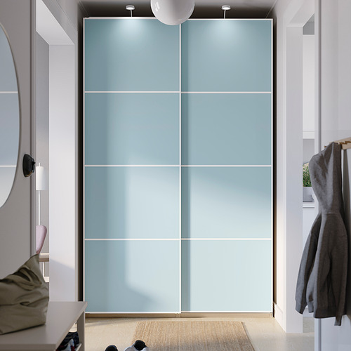 Un armario PAX alto de color azul claro con puertas correderas. El armario es más grande que el espejo y el perchero cercanos, con un diseño elegante y moderno.