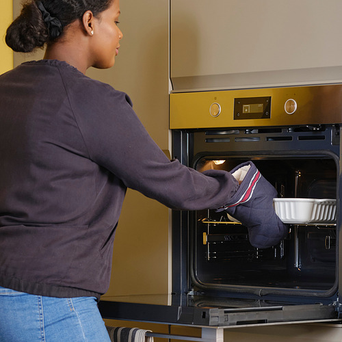 Una mujer usa guantes de cocina para colocar un plato en un horno incorporado.