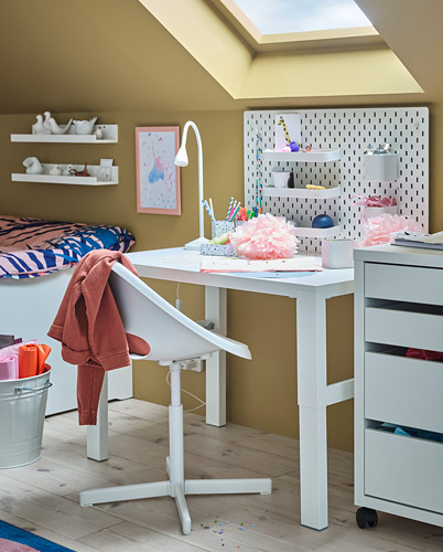 Una zona de estudio bien iluminada con una lámpara NÄVLINGE blanca sobre un escritorio, con una cómoda silla, una decoración colorida y papelería organizada.