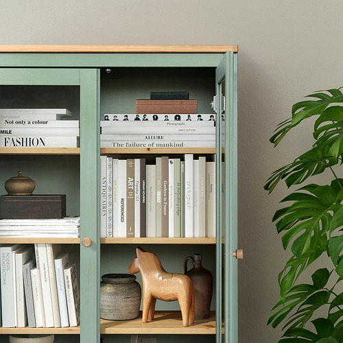 Mueble con puerta de cristal HEMNES verde con estantes ajustables, expositores de libros y caballo de madera. Montado en la pared para mayor estabilidad.