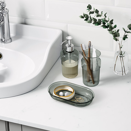 Lavabo de baño con dispensador de jabón, soporte para cepillos de dientes, bandeja y jarrón. Accesorios BROFJÄRDEN cromados sobre encimera.