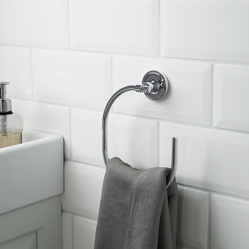 Toallero cromado en la pared alicatada, sosteniendo una toalla gris, parte de los accesorios de baño BROFJÄRDEN.