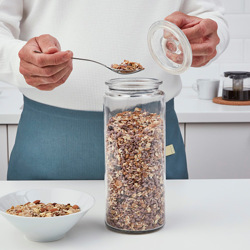 La persona saca granola de un frasco grande de VARDAGEN con una cuchara en un tazón sobre la mesa.