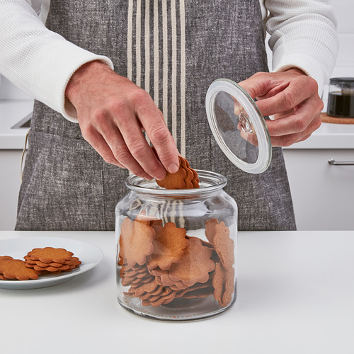 Una persona vierte galletas de un frasco de vidrio transparente en un plato. El frasco, que tiene una tapa con una junta de silicona, muestra las galletas claramente.