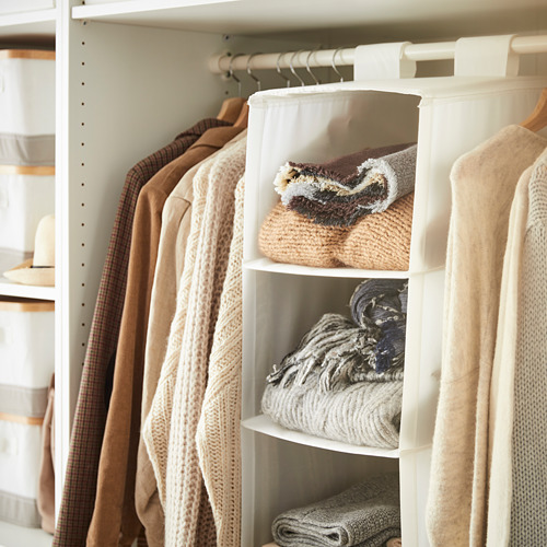 Armario bien organizado con ropa beige; una unidad de almacenamiento colgante etiquetada como SKUBB en blanco sostiene suéteres doblados.