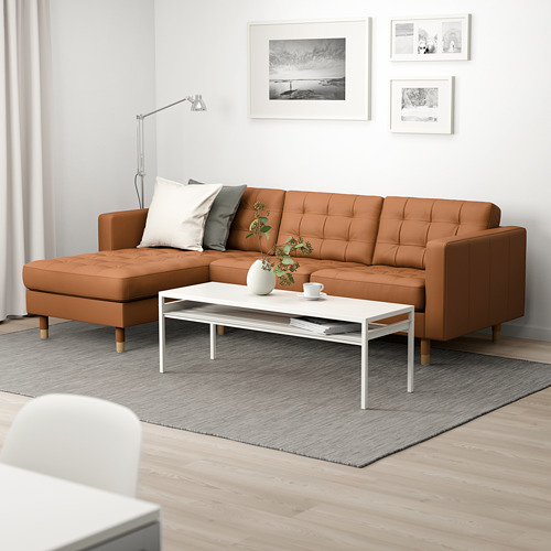 Sala de estar moderna con sofá marrón en forma de L, mesa de centro blanca, alfombra gris, arte de pared y lámpara de pie.