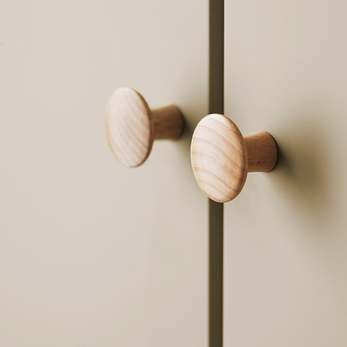 Dos pomos de madera lisa y de color claro montados sobre un armario beige, con un diseño elegante y sencillo.