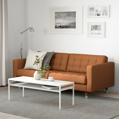 Sala de estar moderna con sofá marrón, mesa de centro y decoración. Incluye jarrón, taza, fotos y lámpara de pie.