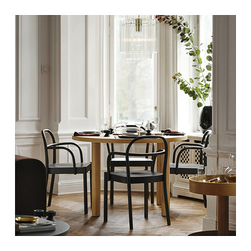Comedor moderno con mesa de chapa de roble y sillas negras, decoradas con vegetación y copas de vino.