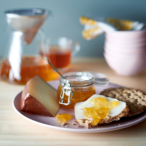 Una fuente con pan, queso, mermelada de naranja y una jarra. VAGGSÅNG naranja y flor de saúco para untar.