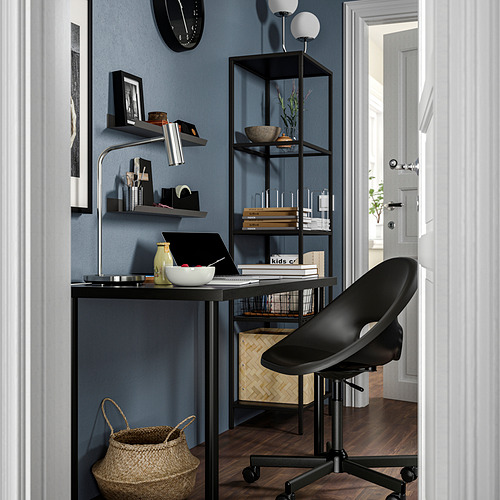 Moderno escritorio de oficina negro con portátil, silla negra, estanterías con libros y decoración, pared azul, cesta de mimbre, diseño minimalista.