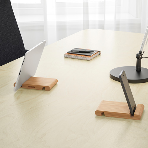Un soporte de madera que sostiene una computadora portátil y una tableta en posición vertical sobre un escritorio. La mesa también tiene un bloc de notas, bolígrafos y un monitor.