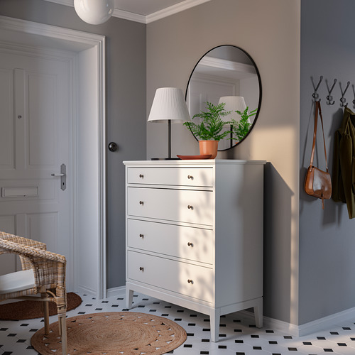 Entrada luminosa con cofre blanco de IDANÄS, espejo negro, lámpara y percheros, paredes grises y azulejos en blanco y negro.