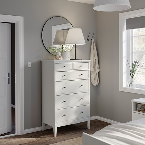 Moderno dormitorio gris con cómoda alta blanca IDANÄS, espejo redondo, lámpara y ventana con persianas.