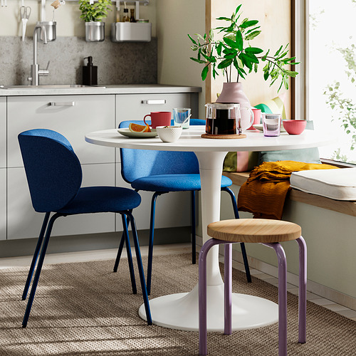 Comedor pequeño y moderno con mesa blanca, sillas KRYLBO azules, plantas y tazas de colores. Espacio de cocina luminoso y acogedor.