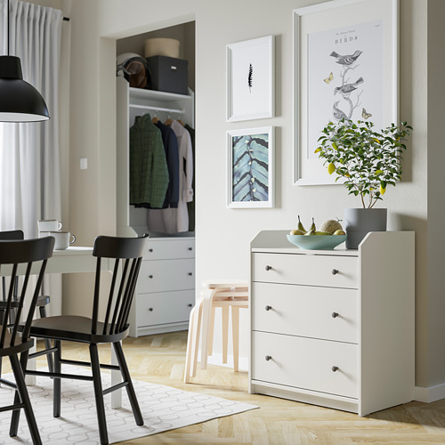 Habitación moderna con cofre HAUGA blanco, sillas negras, arte y planta.