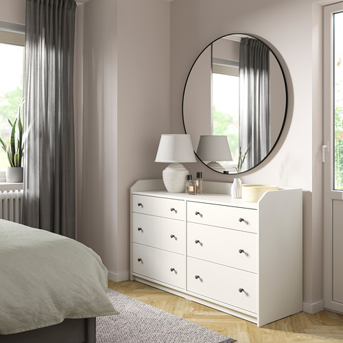 Hermoso dormitorio con tocador HAUGA blanco con seis cajones, espejo redondo, lámparas y paredes rosas.
