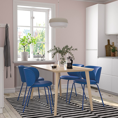Acogedora configuración de comedor con silla azul con mesa de madera, alfombra a rayas, paredes rosas, plantas y vista a la ventana.