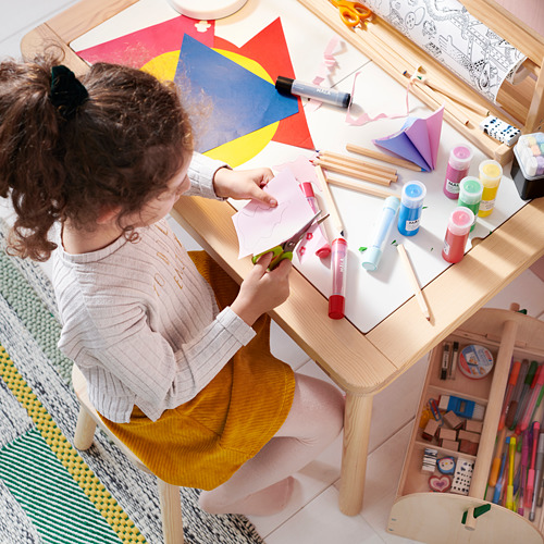 Un niño hace manualidades con papel de colores y pintura en una mesa de madera.