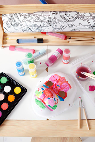 Materiales de arte sobre una mesa: una mariposa pintada, botellas de pintura de varios colores, pinceles y un libro de dibujo.