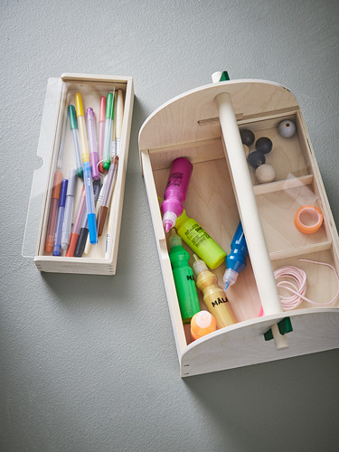 Dos cajas de almacenamiento de madera contra una pared. Uno contiene bolígrafos de colores. El otro tiene materiales de arte, como pinturas, pinceles y cinta adhesiva.