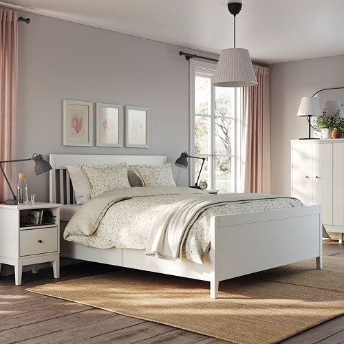 Dormitorio con cama blanca IDANÄS, ropa de cama beige, suelo de madera, cortinas rosas, arte de pared, lámparas y tocador.