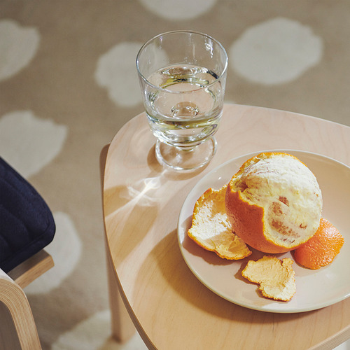 Un vaso de agua descansa sobre una mesa de madera junto a una naranja pelada en un plato.
