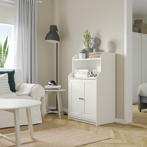 Mueble HAUGA blanco con decoración, planta, lámpara y sillón.