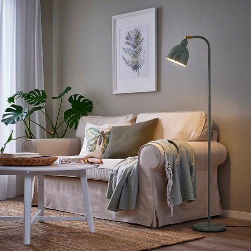 Acogedora sala de estar con lámpara RÖDFLIK que ilumina un sofá beige, mesa de café y arte de hojas.