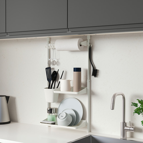 El organizador de pared de cocina SUNNERSTA blanco entre gabinetes sostiene toallas de papel, tazas, platos y utensilios.