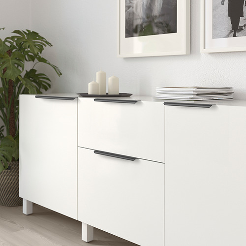 Moderno mueble blanco con manijas oscuras, exhibiendo velas y revistas.