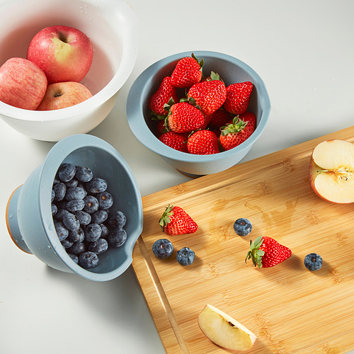 Tres tazones llenos de manzanas, fresas y arándanos. Un cuenco inclinado sobre una tabla de cortar con fruta esparcida.