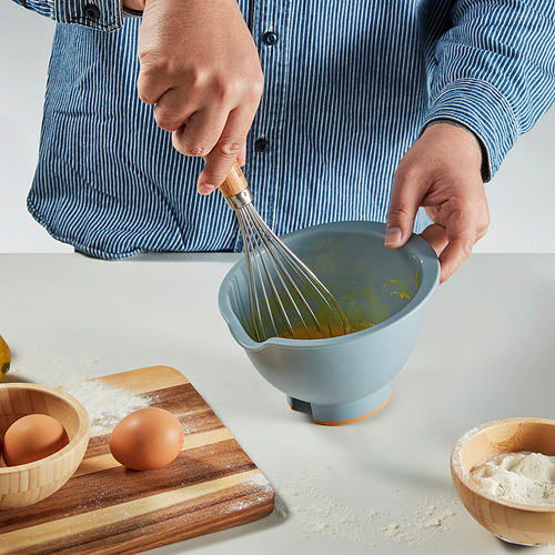 Persona batiendo líquido en un recipiente azul con un pico en una encimera de cocina.