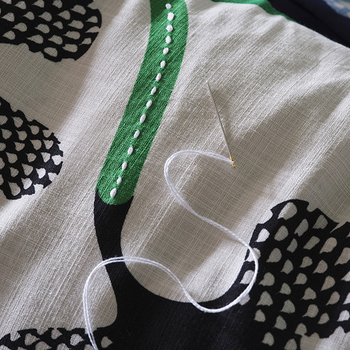 Primer plano de la tela estampada con aguja de coser e hilo, mostrando costuras intrincadas y un diseño detallado.