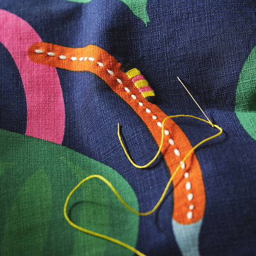 Primer plano de la funda de cojín bordada a mano con oruga naranja y un colorido diseño abstracto, que muestra costuras intrincadas y colores vibrantes.