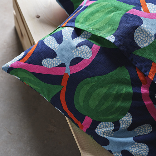 Funda de cojín con dibujos brillantes con manzanas verdes y hojas rosas en una silla de madera. Detalle de oruga bordado a mano en la parte delantera.