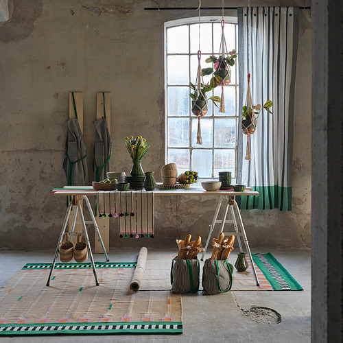 Sala industrial con cortinas de rayas MÄVINN , decoración rústica, mesa de madera con flores y alfombras estampadas.