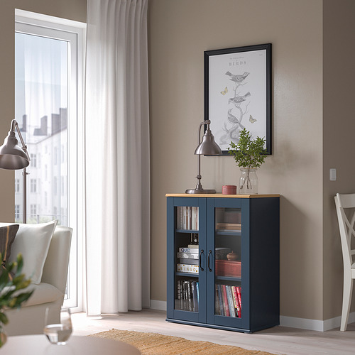 Sala de estar moderna con mueble con puerta de vidrio azul SKRUVBY. Sostiene libros, exhibe decoración. De tamaño perfecto, cabe entre la ventana y la silla.