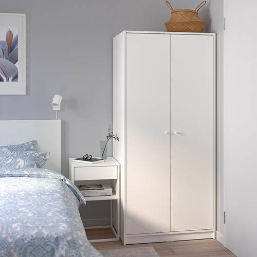 Armario KLEPPSTAD al lado de la cama con ropa de cama azul, cesta, mesita de noche, lámpara, libros y cuadro enmarcado en la pared morada.