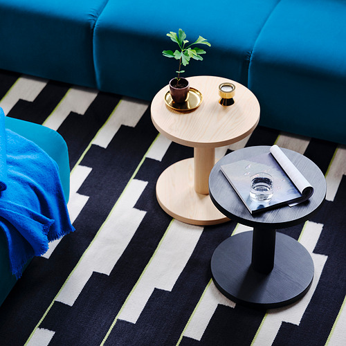 Sofá azul con dos mesas auxiliares. Uno sostiene una planta, el otro tiene un vaso y un cuaderno. Alfombra en zigzag blanco y negro debajo.