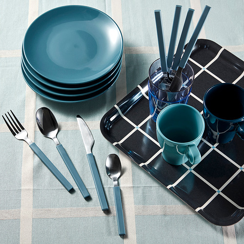 Mesa con platos, tazas y utensilios de color verde azulado. Los cubiertos incluyen tenedor, cuchillo, cuchara y cucharilla, organizados en una bandeja blanca y negra.