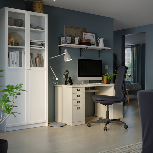 Oficina en casa con librería blanca BILLY, escritorio de madera clara, silla gris, computadora, lámpara y pared verde.