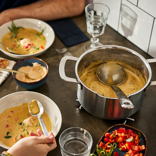Sopa en la estufa con tazones y verduras cerca.