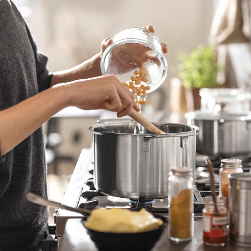 La persona vierte la pasta en una olla grande con una tapa de colador en una estufa. En las inmediaciones hay varias especias y un cuenco.