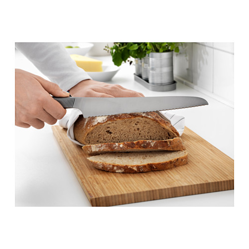 Persona cortando pan con un cuchillo de sierra sobre una tabla de cortar de madera.