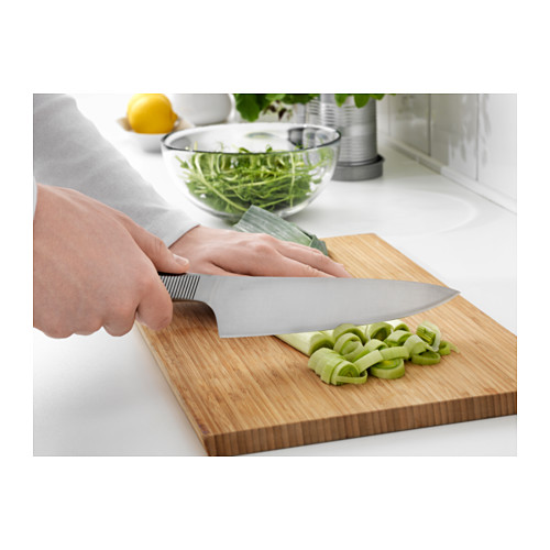 Persona cortando verduras verdes en una tabla de cortar de madera con un cuchillo de cocina grande.