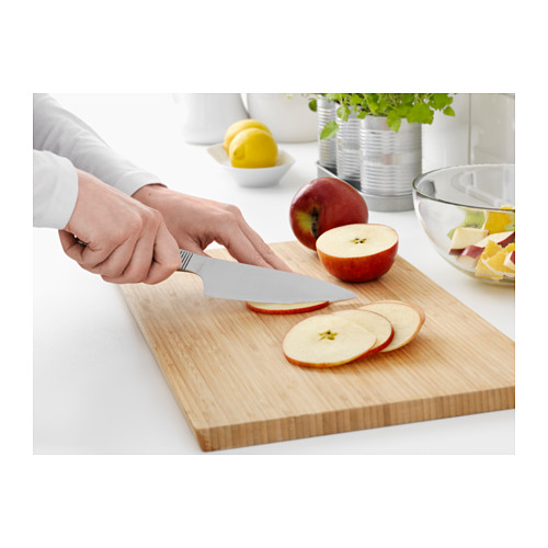 Manos cortando manzana en tablero de madera para cuchillos ikea, cuchillo de acero inoxidable, cuenco de fruta cerca.