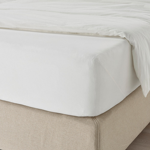 Una cama cuidadosamente hecha con una sábana bajera DVALA blanca, que muestra su borde elástico y su suave textura de algodón.