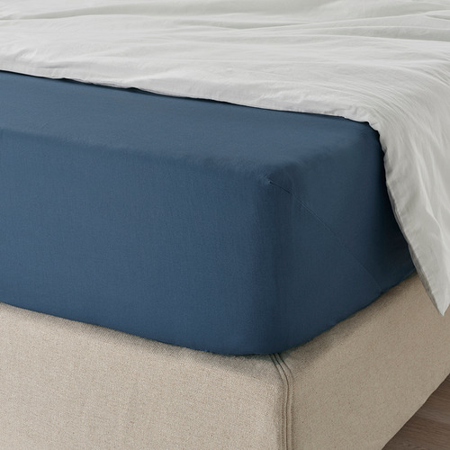Cama cuidadosamente hecha con sábana azul oscuro, bordes elásticos, textura suave.