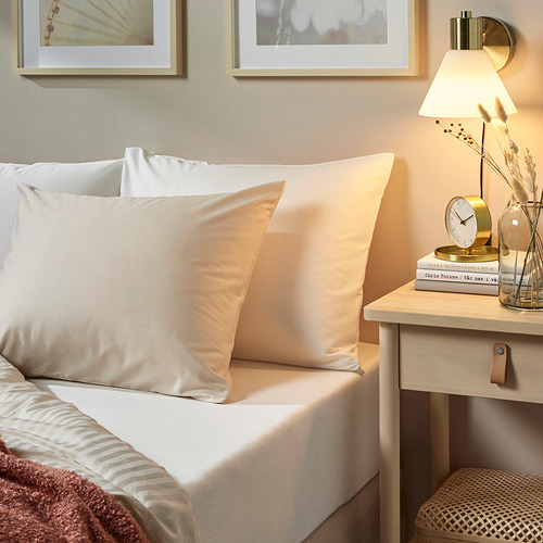 Funda de almohada marfil en la cama, lámpara dorada, decoración minimalista.